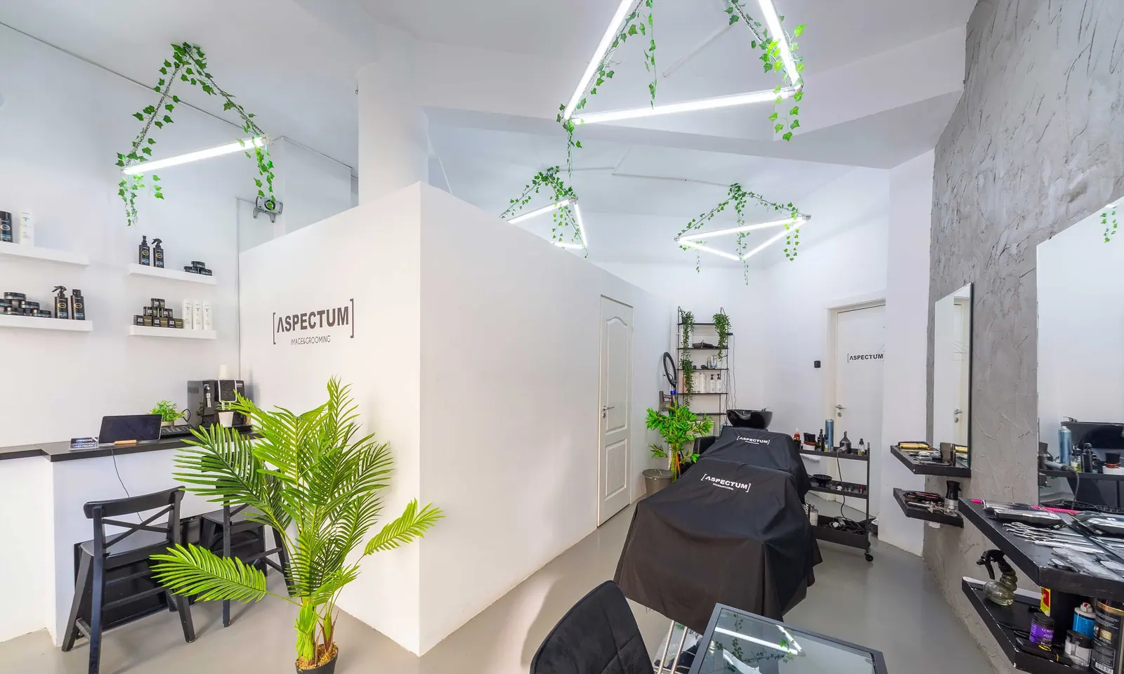Interiorul salonului ΛSPECTUM din București: scaune de frizerie, oglinzi cu ramă neagră și raftul Balmain